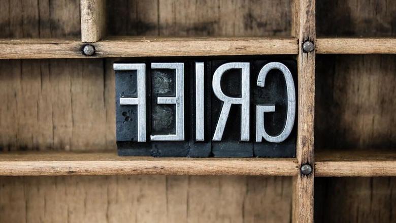 The image shows the word GRIEF spelled out in metal letterpress blocks placed within a wooden compartment, 催人奋进, 忧郁的情绪.